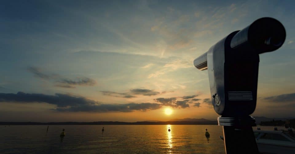 Telescope overlooking water at sunset for celestial observation.