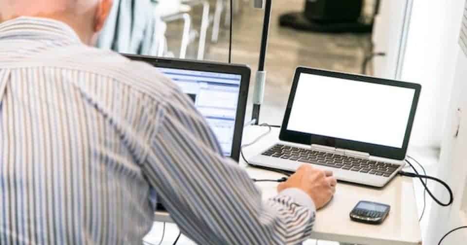 Person working on dual laptops with smartphone on desk.
