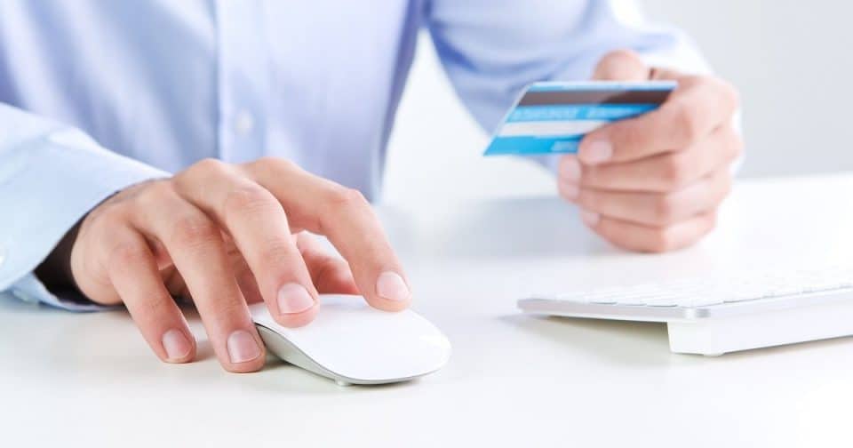 Person using a credit card and mouse for online retail transaction.