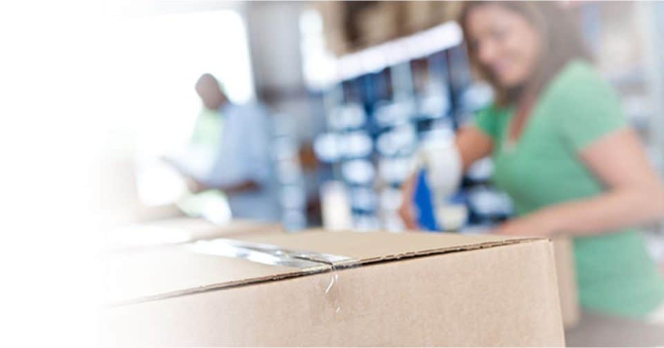 Warehouse worker in green shirt handling a cardboard box in a logistics facility.